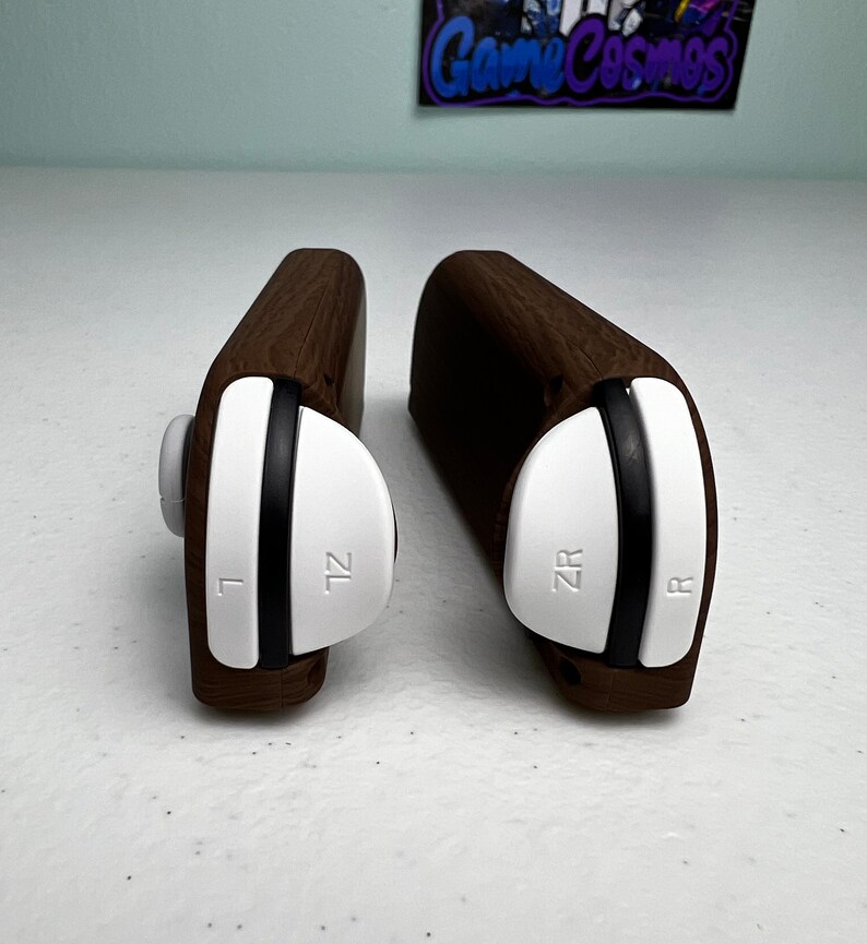 May include: Two wooden controller grips for the Nintendo Switch. The grips are brown and have white buttons labeled "ZL" and "ZR" on the left and right grips, respectively.