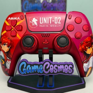 May include: A red wireless gaming controller featuring anime-style character illustrations, the text ASUKA, UNIT-02, PROJECT EVA - TOKYO 03, and the NERV logo. The controller has black analog sticks, a central PlayStation logo, and red buttons.