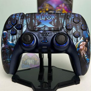 Op de afbeelding: Een aangepaste PlayStation 5-controller met een donkerblauwe afwerking en een bosachtergrond. Het centrale touchpad toont de tekst Weapon X. Deadpool staat op de linkerhandgreep en Wolverine op de rechterhandgreep. De knoppen zijn zwart.