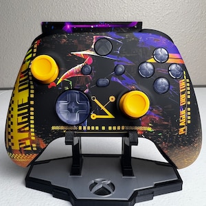 May include: A black and yellow Xbox controller with a custom design featuring a purple and black background with a graphic of a character from the video game "Plague Doctor". The controller is on a black stand with a silver Xbox logo.