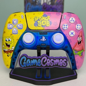 May include: A custom video game controller featuring a yellow left side with SpongeBob SquarePants and a pink right side with Patrick Star. The center touchpad displays the SpongeBob logo, and the controller is mounted on a black GameCosmos stand.