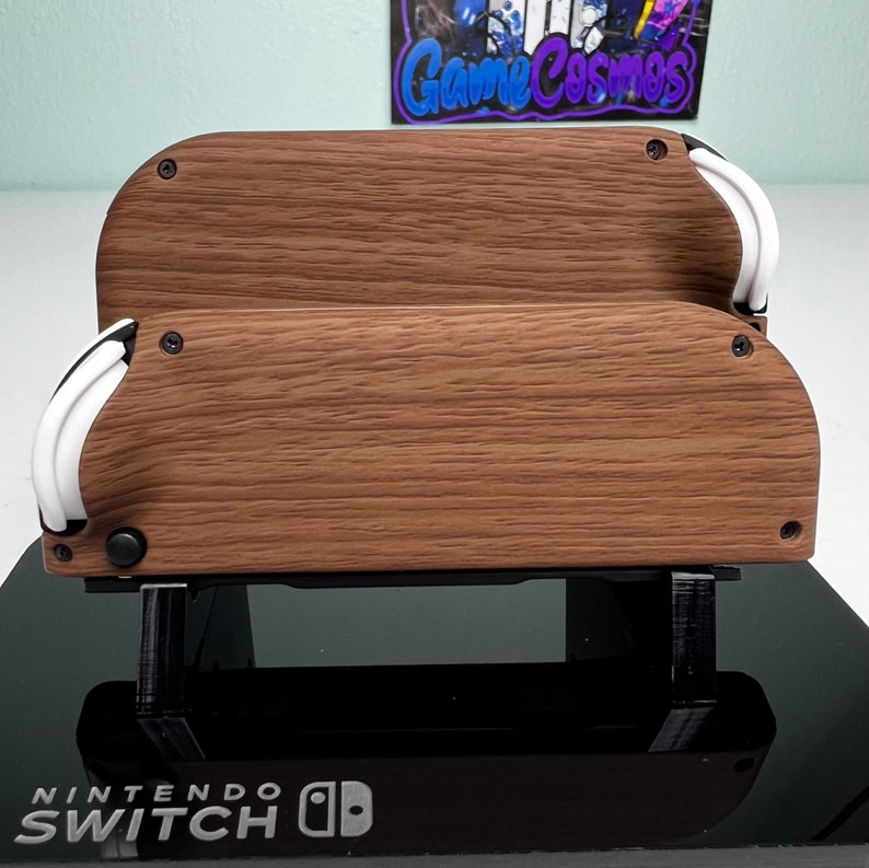 May include: A wooden Nintendo Switch dock stand with a textured wood grain finish. The stand has two levels and a white accent on the front. The stand is sitting on a black surface with the text "NINTENDO SWITCH" printed on it.