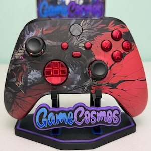 May include: Custom Xbox controller featuring a dragon design in black and red. The controller has red buttons and thumbsticks, and is displayed on a stand with the text "Game Cosmos".