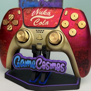 May include: A custom video game controller featuring a red and gold weathered finish with the text Nuka Cola printed on the center touchpad. The controller includes gold-colored buttons, joysticks, and bullet-style action buttons.