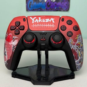 May include: A red and black wireless game controller featuring The Yakuza Remastered Collection branding on the center touchpad. The controller displays a koi fish graphic on the left side and a dragon illustration on the right side.