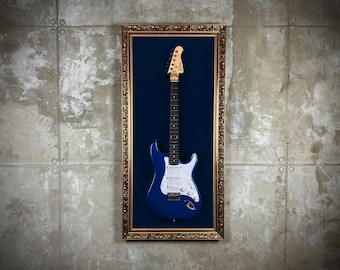 May include: A blue electric guitar with white accents is displayed in a gold-colored frame with a blue velvet background.