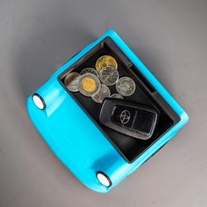 May include: A blue toy car with a black interior. The car has a small compartment in the back that is filled with coins and a black car key with the word "COROLLA" printed on it.