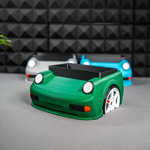 May include: Three car-shaped desk organizers, one green, one blue, and one gray. The green organizer is in focus and has a black interior.
