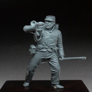 Puede incluir: Un modelo de plástico gris de un soldado de la época de la Guerra Civil estadounidense en uniforme, sosteniendo una trompeta y una espada. El soldado lleva un sombrero y tiene barba.