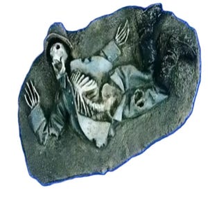 Puede incluir: Una figura esquelética con un sombrero y ropa está incrustada en una superficie rocosa. La figura parece estar acostada de espaldas con los brazos extendidos.