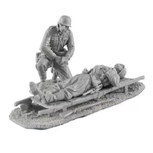 Op de afbeelding: Een grijs plastic model van een Duitse soldaat die een andere gewonde soldaat helpt op een brancard te klimmen. De soldaat draagt een helm en een uniform. De brancard is van hout en heeft een canvas bovenkant.