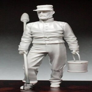 May include: A light gray figurine of a man in a military uniform, holding a bucket and a tool. The figure is wearing a hat and has a beard. The uniform includes a jacket and pants. The bucket has a handle.
