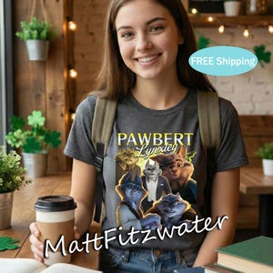 以下が含まれることがあります： 「PAWBERT Lynxleg」の文字と擬人化されたオオヤマネコのグラフィックが特徴の濃い灰色のTシャツ。シャツの下部には「MattFitzwater」の文字も。人物はバックパックを背負い、コーヒーカップを持っています。