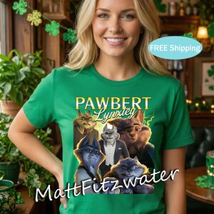 以下が含まれることがあります： 「PAWBERT Lynxley」の文字と漫画の猫のグラフィックが特徴の緑色のTシャツ。シャツの下部には「MattFitzwater」の文字も入っています。Tシャツは人が着ています。
