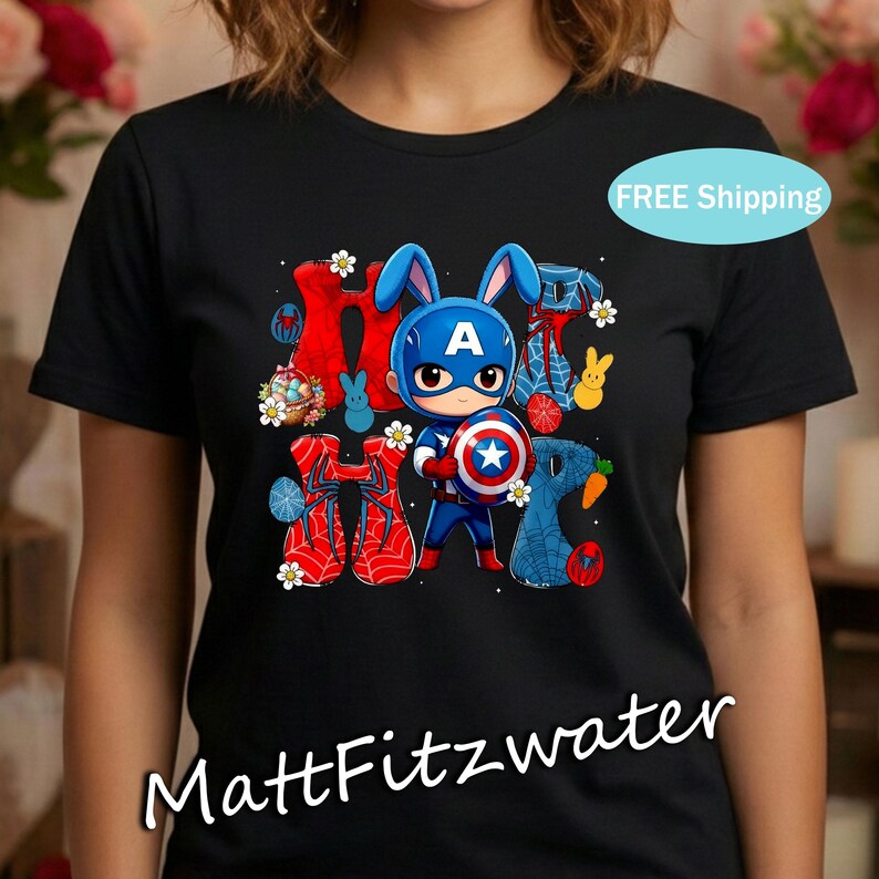 Pu&ograve; includere: T-shirt nera con un personaggio dei cartoni animati di Capitan America con orecchie da coniglio e uno scudo. La parola "Hoppy" &egrave; visualizzata in un carattere colorato con decorazioni pasquali. Il testo "MattFitzwater" &egrave; in basso.