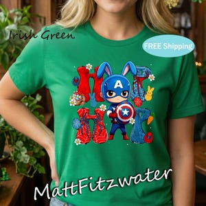Pu&ograve; includere: T-shirt verde con la scritta "Irish Green" e "MattFitzwater". La maglietta presenta una grafica di Capitan America come un coniglietto con la parola "HOP" ed elementi a tema pasquale.