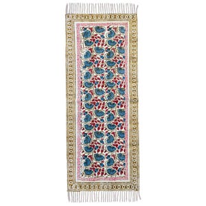 Puede incluir: Un camino de mesa rectangular blanquecino con un estampado floral. El diseño presenta flores azules y hojas rojas sobre un fondo blanco, enmarcado por un borde rosa y un borde marrón con un patrón circular. El camino de mesa tiene flecos en ambos extremos.