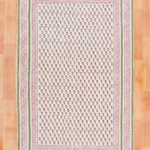 Puede incluir: Una alfombra de algodón blanco con un patrón floral verde y rosa. La alfombra tiene un borde de flecos.