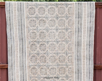 Puede incluir: Una alfombra de algodón blanco con un patrón geométrico negro y gris. La alfombra tiene un borde de flecos y está colgada en una valla de metal roja. El texto "@Nilesh Arts" está impreso en la alfombra.