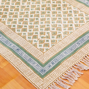 Puede incluir: Una alfombra de color blanco, verde y marrón con un diseño geométrico. La alfombra tiene un borde de flecos y está hecha de algodón.