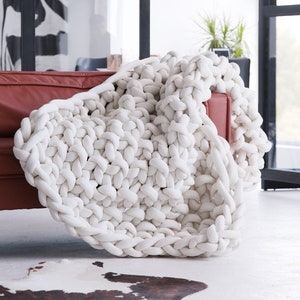 Peut inclure: Une couverture en tricot blanc épaisse et moelleuse drapé sur un canapé en cuir rouge. La couverture est faite de fil épais et doux et a un aspect décontracté et décontracté.