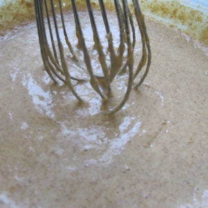 Puede incluir: Primer plano de una masa de color marr&oacute;n claro que se mezcla en un bol con un batidor. La masa es suave y cremosa, y el batidor es de metal.