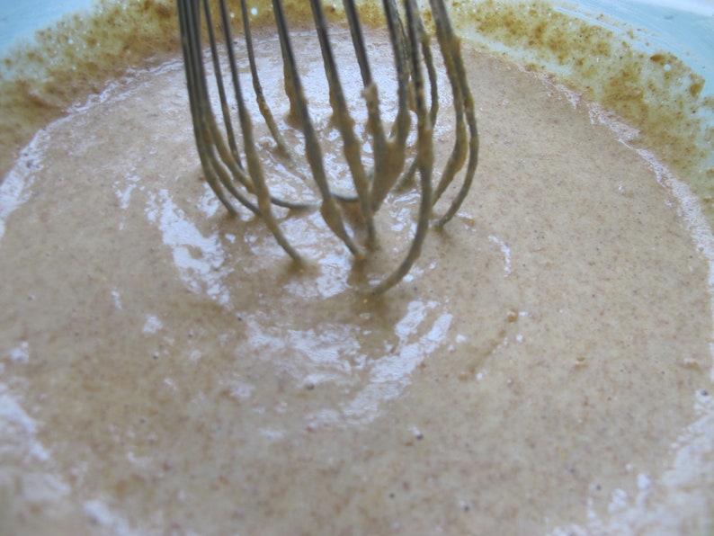 Puede incluir: Primer plano de una masa de color marr&oacute;n claro que se mezcla en un bol con un batidor. La masa es suave y cremosa, y el batidor es de metal.