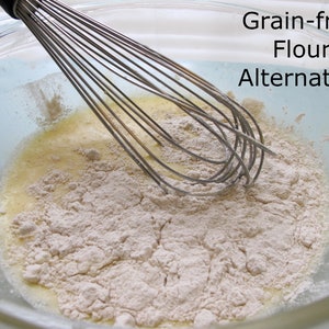 Puede incluir: Primer plano de un bol de vidrio con un batidor de alambre y un polvo blanco. El texto "Grain-free Flour Alternative" est&aacute; escrito en el lado derecho de la imagen.