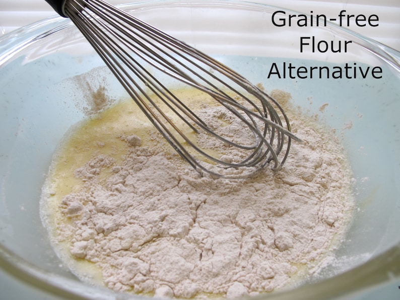 Puede incluir: Primer plano de un bol de vidrio con un batidor de alambre y un polvo blanco. El texto "Grain-free Flour Alternative" est&aacute; escrito en el lado derecho de la imagen.