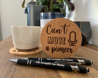 May include: Cork coaster with the text "Can't mute a pioneer" and a microphone icon. The coaster is on a wooden surface with two black pens that say "Fully Accomplish Your Ministry".