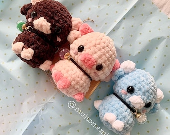 Könnte beinhalten: Drei gehäkelte Tierplüschtiere in Braun, Rosa und Blau. Das braune Plüschtier hat ein weißes Gesicht und schwarze Augen. Das rosa Plüschtier hat ein rosa Gesicht und schwarze Augen. Das blaue Plüschtier hat ein weißes Gesicht und schwarze Augen. Die Plüschtiere befinden sich auf einem weißen Hintergrund mit kleinen grünen Punkten.