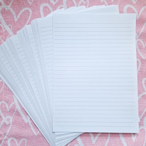 May include: A stack of white lined paper sheets on a pink background with a heart pattern.