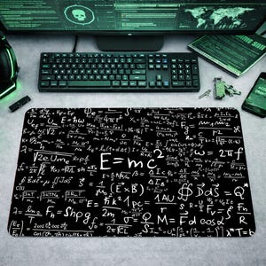 Op de afbeelding: Zwarte muismat met witte wiskundige vergelijkingen, waaronder "E=mc²". De werkplek omvat een computermonitor, toetsenbord, koptelefoon, muis en een smartphone met "ACCESS GRANTED".