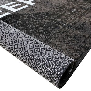 May include: Close-up of a black and white rug rolled up, showing the detailed pattern of the border. The rug has a distressed, vintage look.