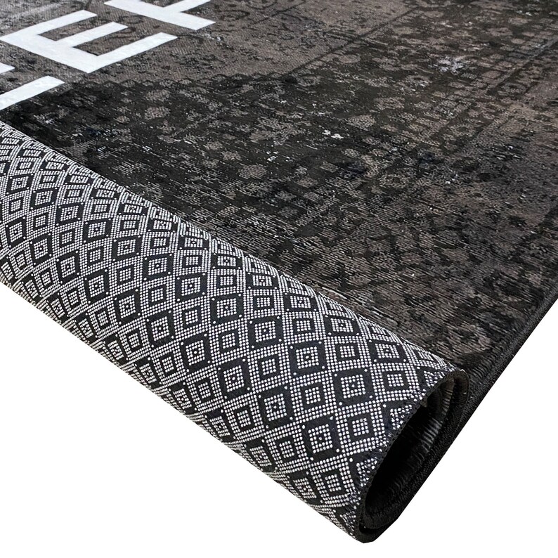 May include: Close-up of a black and white rug rolled up, showing the detailed pattern of the border. The rug has a distressed, vintage look.