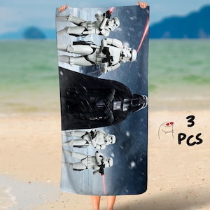Può includere: Un asciugamano da spiaggia con un gruppo di Stormtrooper di Star Wars, con Darth Vader sullo sfondo. L'asciugamano è blu e bianco con un effetto neve. Il testo "3 PCS" è visibile nell'angolo in basso a destra.