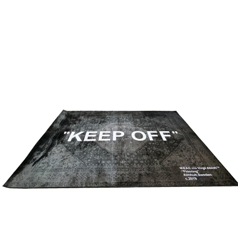 May include: A black and white rug with a distressed pattern and the text "KEEP OFF" in white. The rug also has the text "IKEA clo Virgil Abloh&trade;" "Flooring" "Almhult, Sweden" "c.2019" in white.