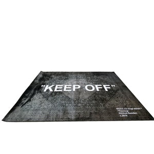 May include: A black and white rug with a distressed pattern and the text "KEEP OFF" in white. The rug also has the text "IKEA clo Virgil Abloh&trade;" "Flooring" "Almhult, Sweden" "c.2019" in white.