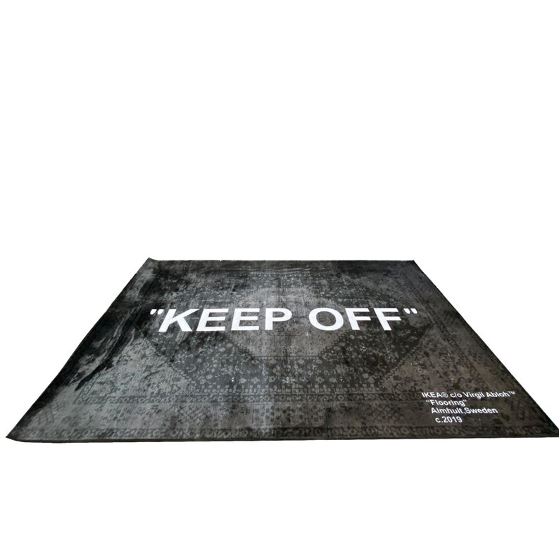 May include: A black and white rug with a distressed pattern and the text "KEEP OFF" in white. The rug also has the text "IKEA clo Virgil Abloh&trade;" "Flooring" "Almhult, Sweden" "c.2019" in white.