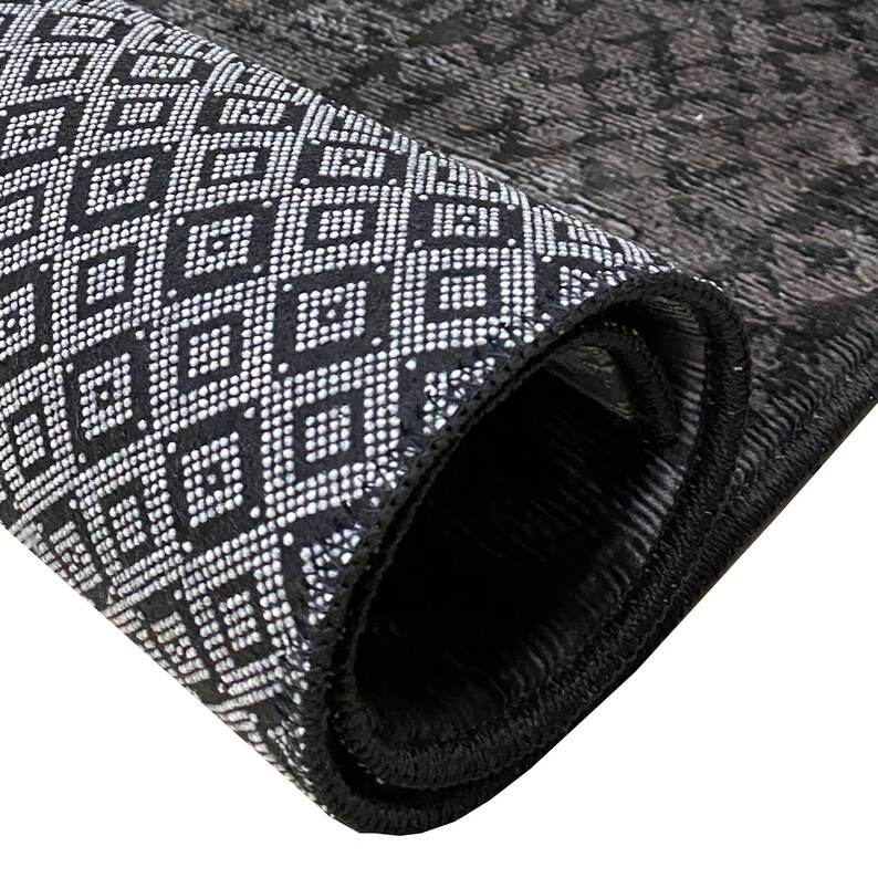 May include: Close-up of a black and white patterned rug with a black border. The rug is rolled up, showing the underside of the fabric.