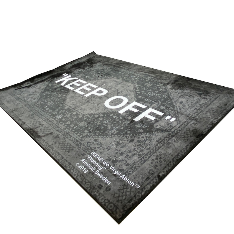 May include: A black and white rug with a vintage pattern and the text "KEEP OFF" in white. The rug is labeled "IKEA&reg; c/o Virgil Abloh&trade;" and "Flooring" with the location "Almhult, Sweden" and the year "c. 2019".