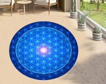 Op de afbeelding: Een rond blauw en wit tapijt met een geometrisch patroon van een levensbloemontwerp. Het tapijt heeft een gloeiend blauw en roze centrum.