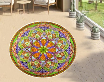 Op de afbeelding: Een rond, kleurrijk mandala-kleed met een groen, oranje, paars en geel ontwerp. Het kleed heeft een witte rand en ligt op een houten vloer.