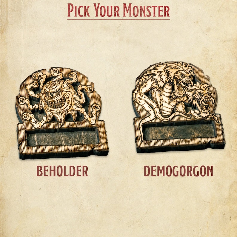 May include: Two wooden plaques featuring monster illustrations. The plaque on the left depicts a beholder with a central eye and numerous tentacles. The plaque on the right shows a demon with a dragon-like head and a snarling face. Both plaques have a blank space for text. The text below the plaques reads "BEHOLDER" and "DEMOGORGON".