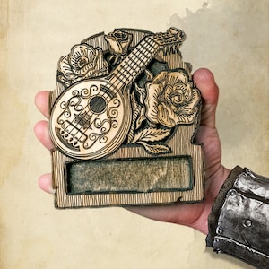 May include: A wooden plaque featuring a carved design of a lute, roses, and a blank space for text. The plaque is brown and has a distressed look.