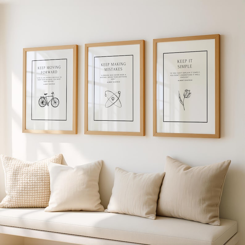 K&ouml;nnte beinhalten: Drei gerahmte Kunstdrucke mit inspirierenden Zitaten. Die Rahmen sind aus hellem Holz, mit wei&szlig;em Hintergrund und schwarzen Texten und Illustrationen. Darunter liegen drei Kissen auf einer wei&szlig;en Bank.