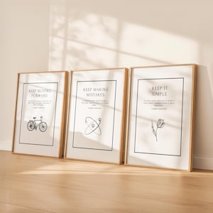 May include: Three framed art prints with inspirational quotes. The prints have a white background with black text and illustrations. The frames are a light brown color. The quotes are "Keep Moving Forward", "Keep Making Mistakes", and "Keep It Simple".