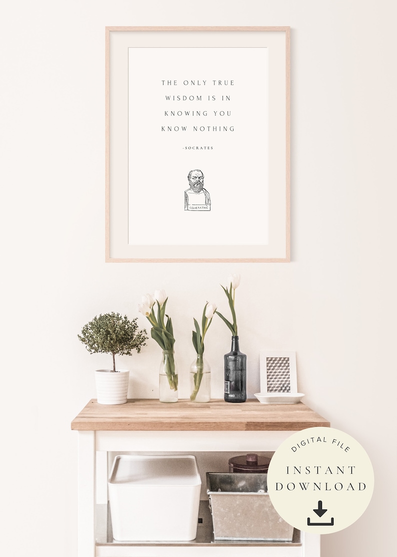 May include: A printable quote by Socrates in a white frame on a white wall. The quote reads "The only true wisdom is in knowing you know nothing - Socrates". A bust of Socrates is pictured below the quote. The image also shows a wooden table with white flowers in vases, a small potted plant, and a decorative tray.
