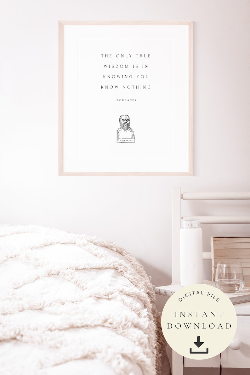 May include: A printable quote by Socrates, "The only true wisdom is in knowing you know nothing." The quote is printed in black text on a white background with a black and white illustration of Socrates below the quote. The quote is framed in a light wood frame and is hanging on a white wall.