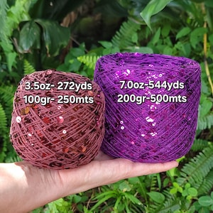May include: Two balls of yarn with sequins, one in a deep maroon and one in a vibrant purple. The maroon ball is labeled 3.5oz- 272yds and 100gr- 250mts. The purple ball is labeled 7.0oz- 544yds and 200gr- 500mts. Both are textured with shiny discs.